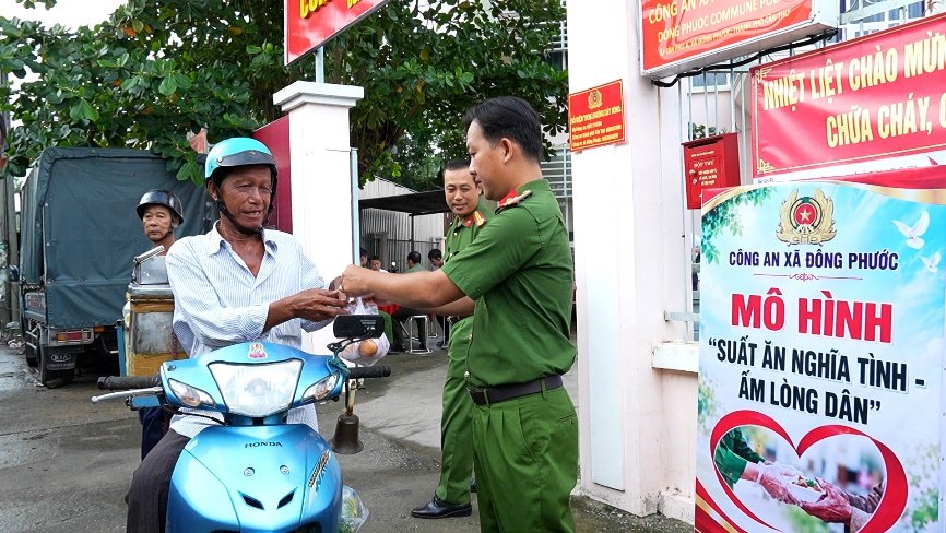 Cán bộ Công an xã Đông Phước ân cần trao phần ăn nghĩa tình cho chú Trần Văn Lâm ngay trước cổng trụ sở.